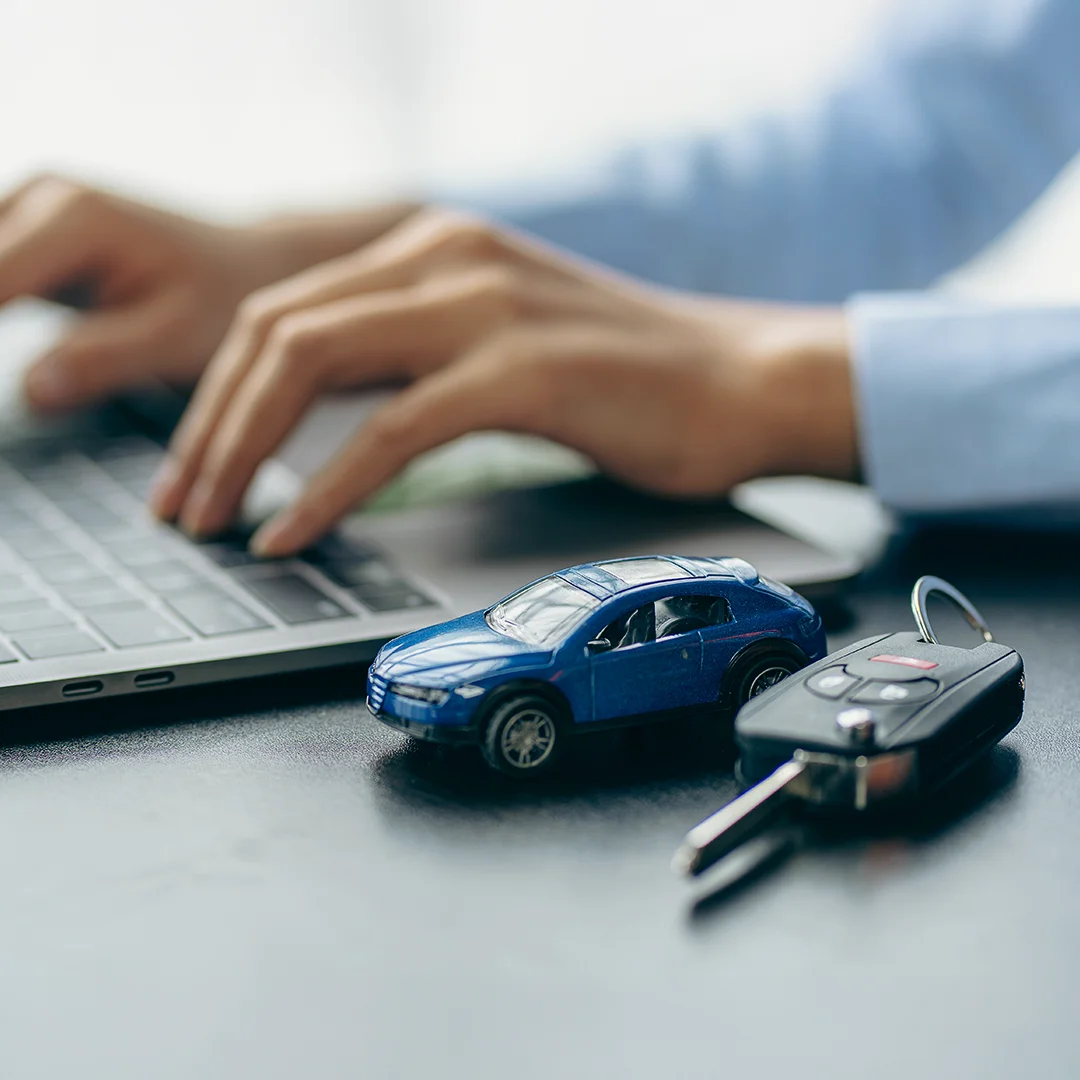 insurance broker typing on a computer with toy car and keys in front of him